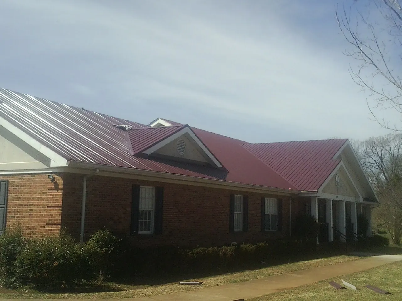 Red metal roof with gabled entries on a long brick building, from a Hail Damage Roof Repair job in Suitland