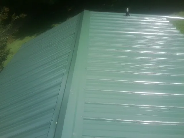 New green metal panels meeting at the ridge of a roof — Flat Roof Repair work by our crew in Suitland