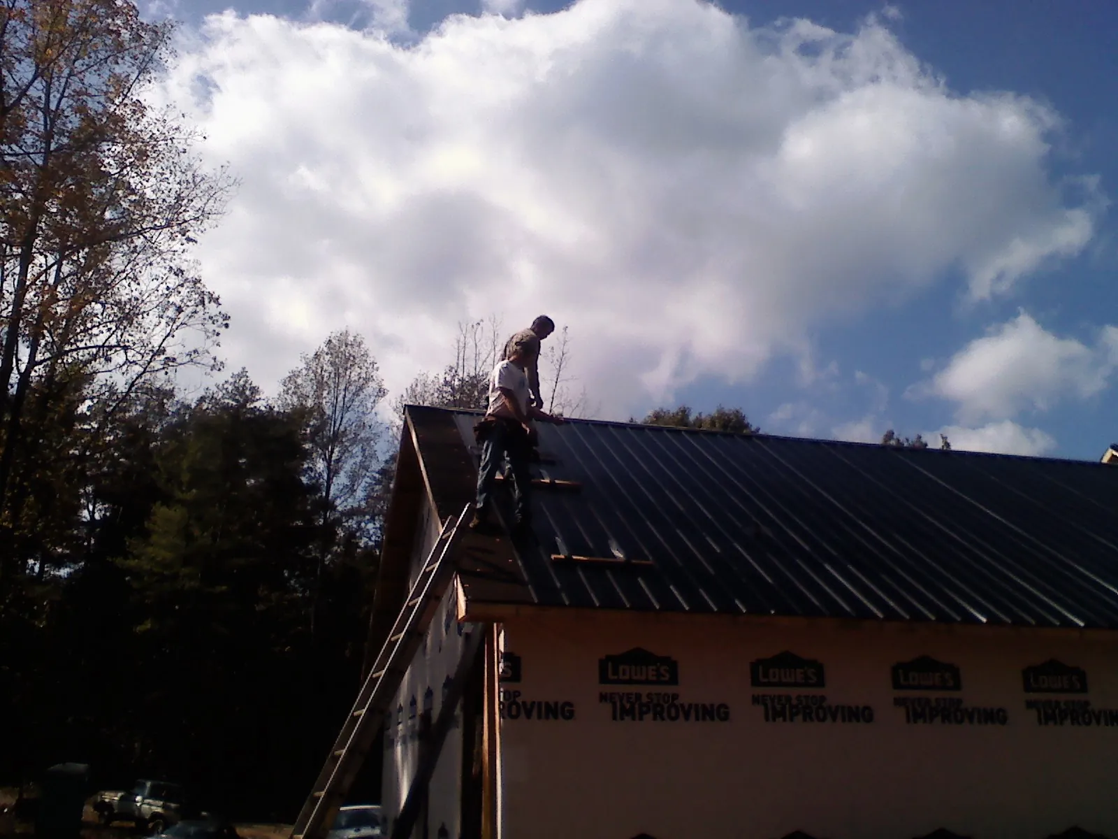 Roofer fastening dark metal panels high against a cloudy sky, from a Roof Inspection job in Suitland