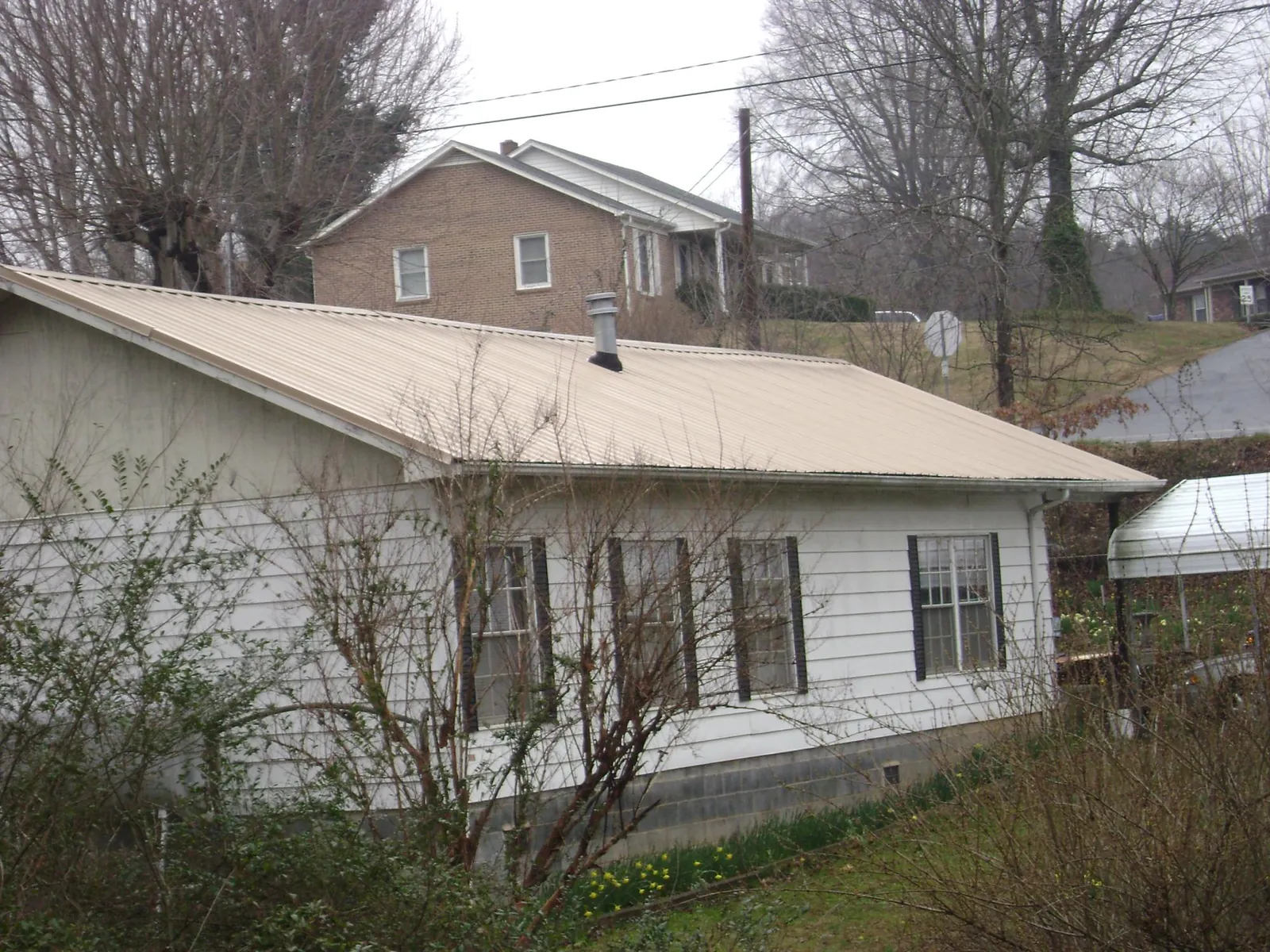 Tan metal roof on a white sided house set into a hillside — Commercial Roofing by Roofing Brothers in Suitland